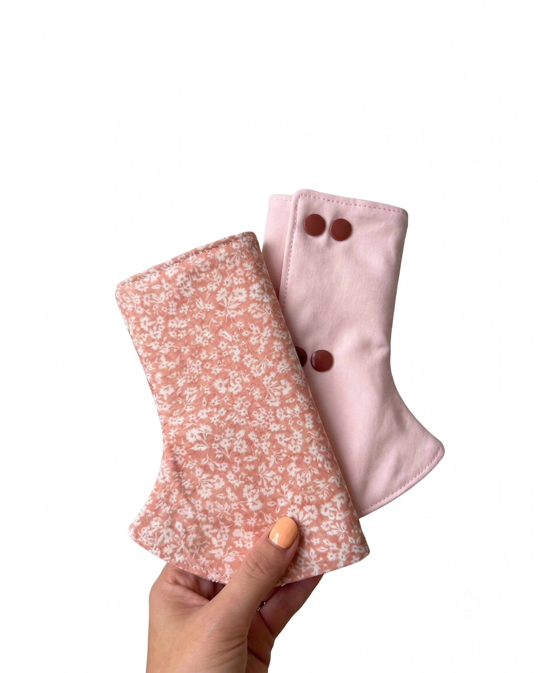 Two pink fabric suck drool pads for baby carrier with floral pattern and button details held by a hand on a white background