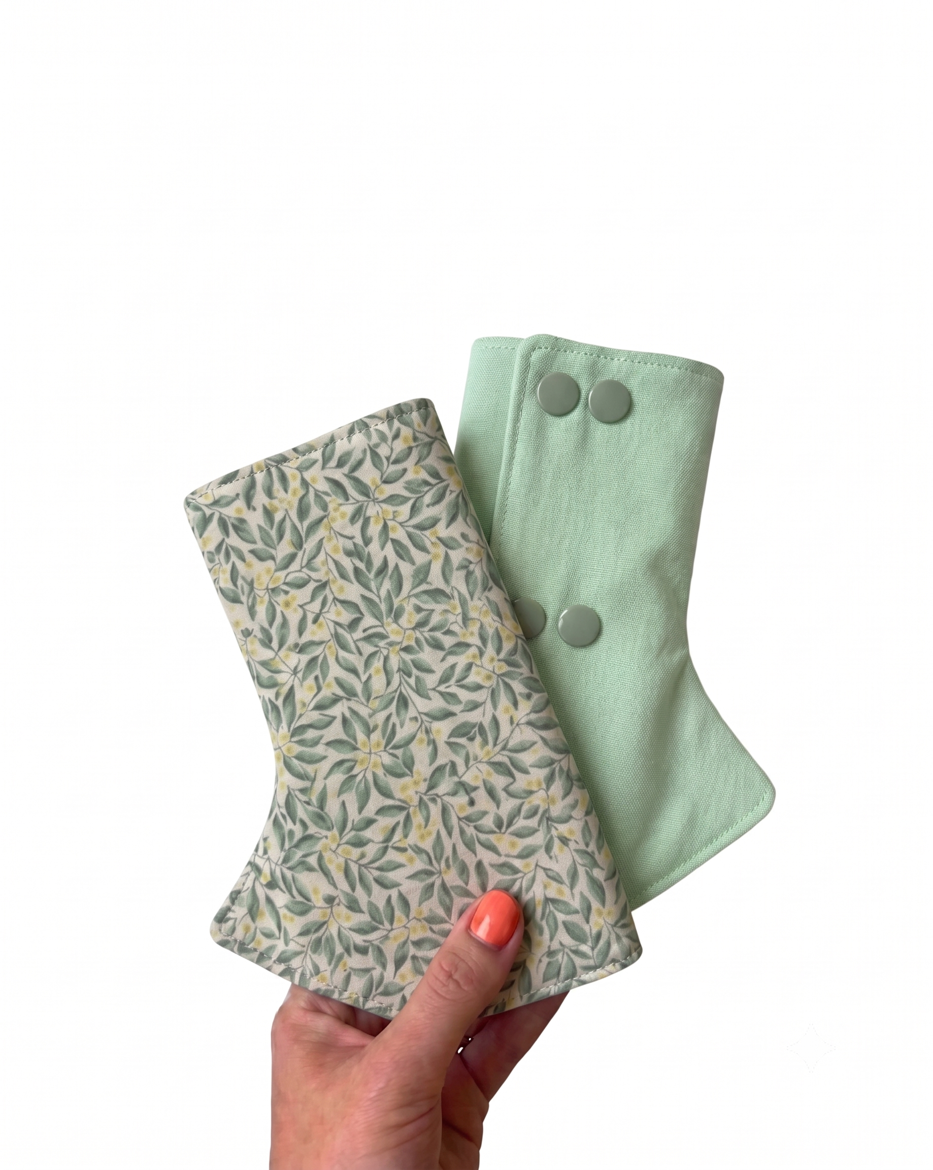 Two green fabric drool pads, one with a leaf pattern, held by a hand on a white background.