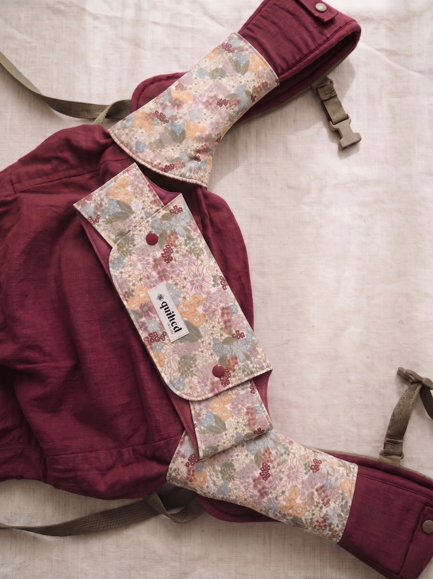 Maroon baby carrier with floral suck pads on a light gray background