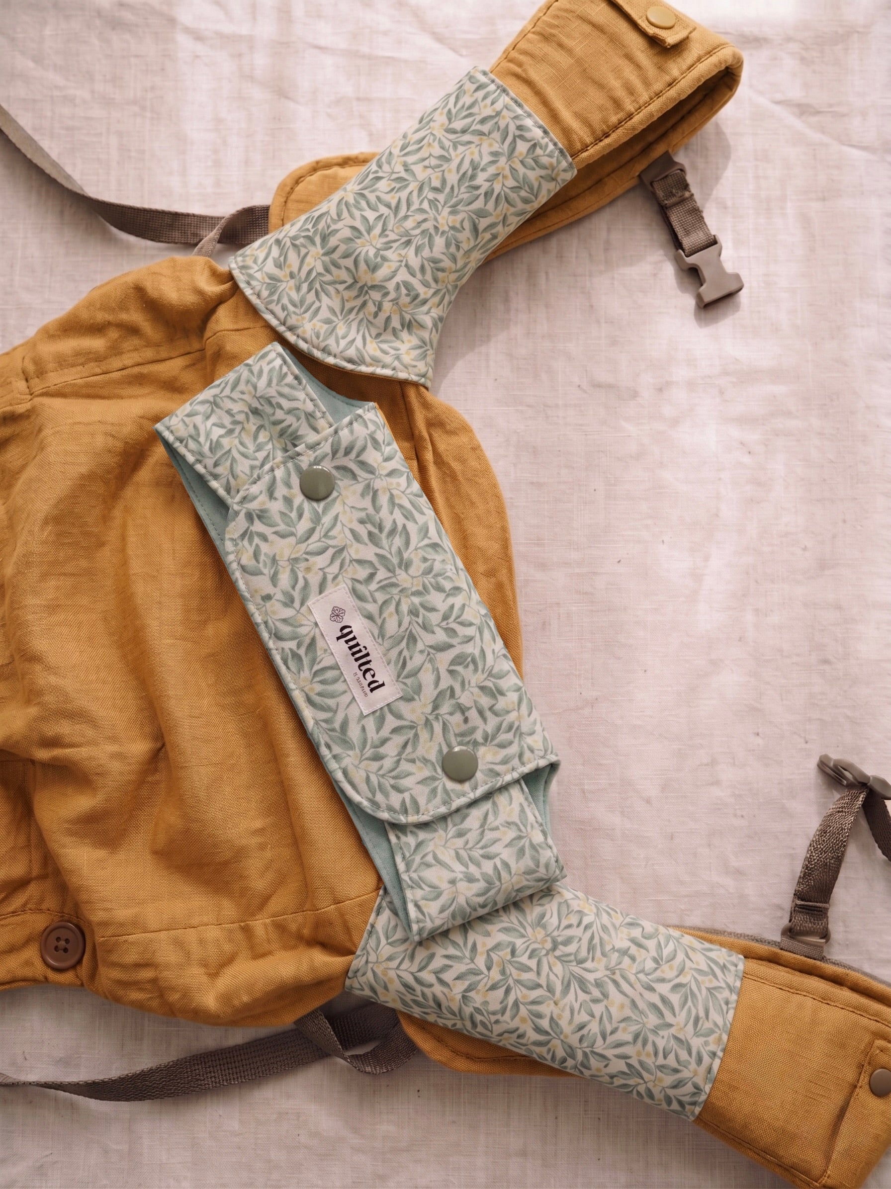 Brown baby carrier with green floral suckpads on a light gray background