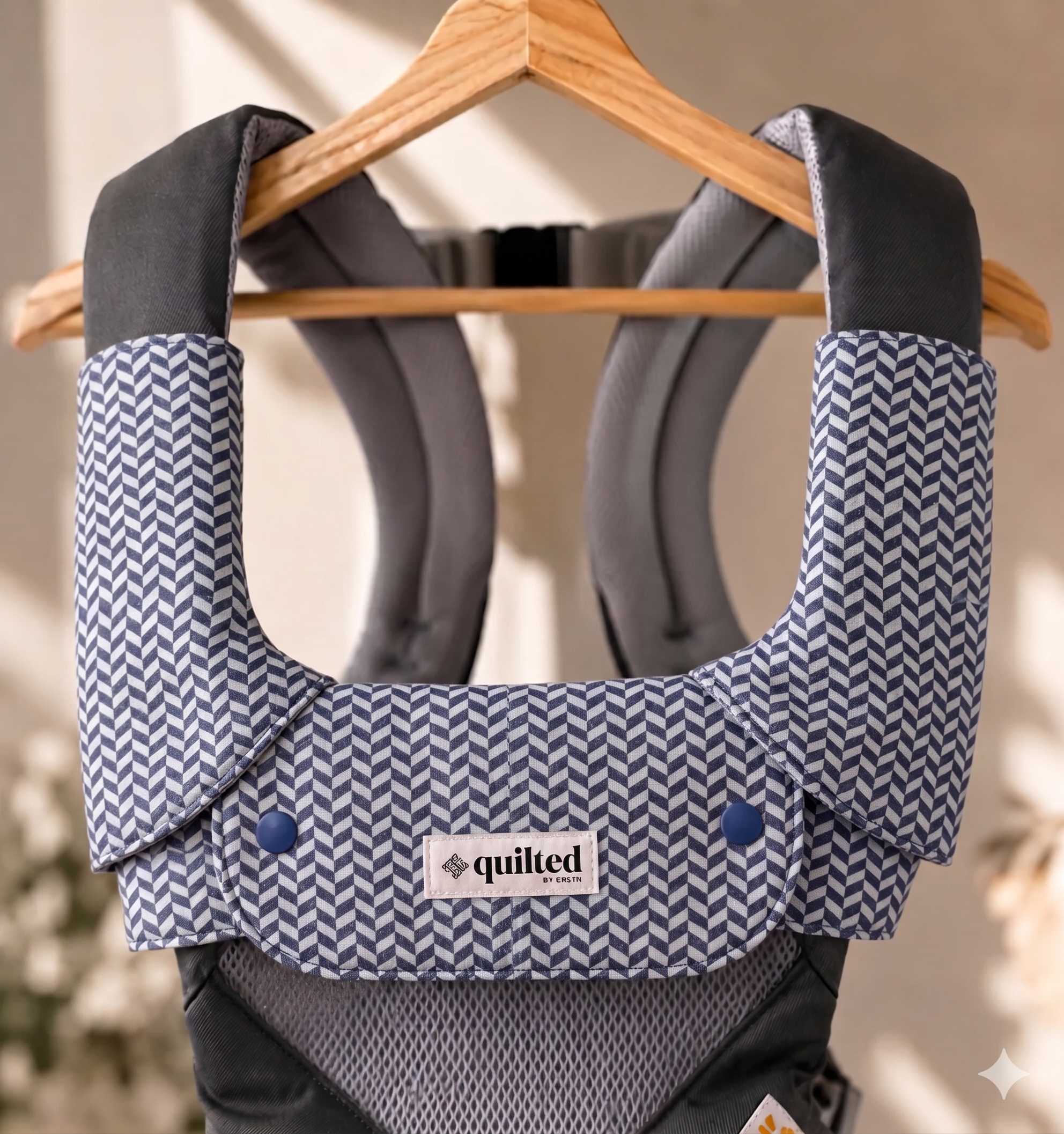 Baby carrier with blue and white pattern on a hanger, featuring 'quilted' brand label.